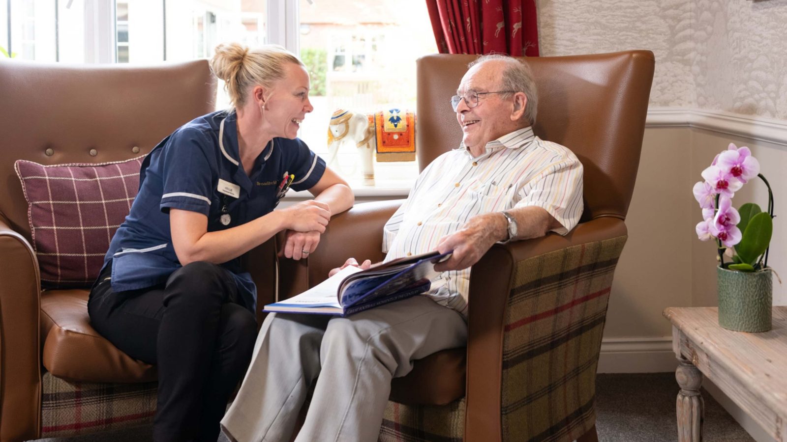 A nurse and a care home resident laughing together in armchairs