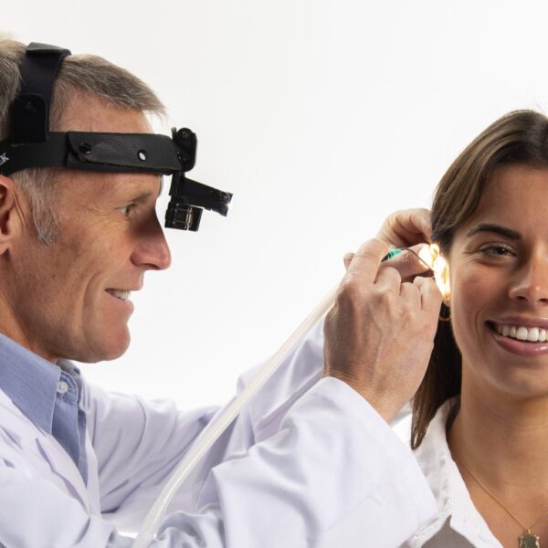 A clinician wearing magnifying loupes gently removes earwax from a smiling client's ear using microsuction
