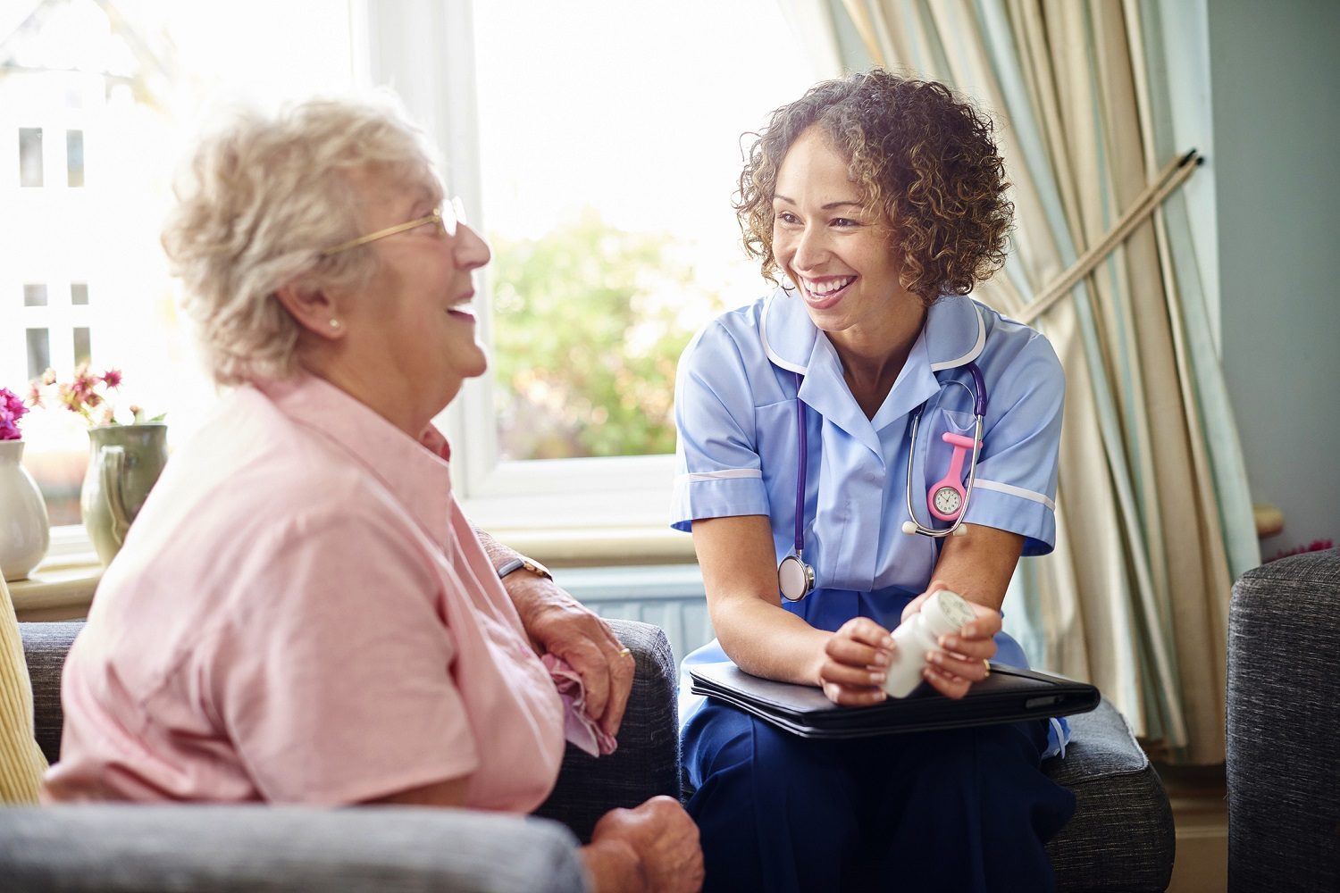 A nurse visiting an older woman at home, both smiling