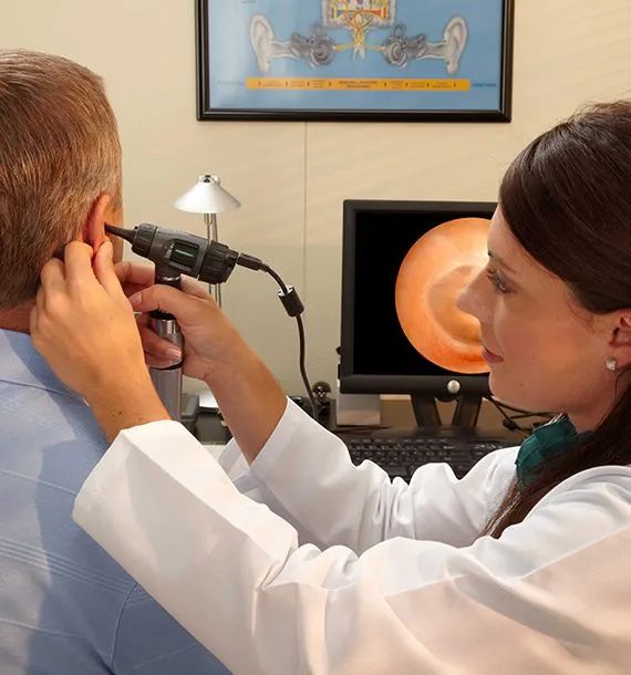 A clinician examines a client's ear with a video otoscope, with the ear canal shown on a screen
