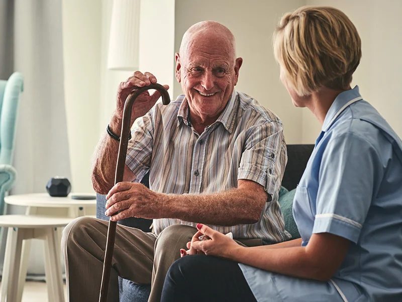 An older man with a walking stick chatting with a carer